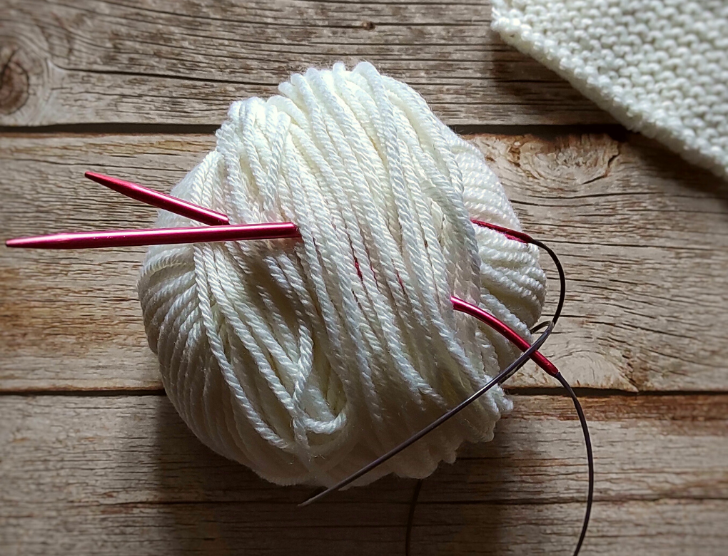 Lavorare a maglia un gomitolo di lana bianco e ferri